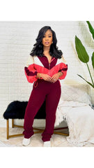 A woman wearing a red and white color-blocked zip-up tracksuit with matching maroon pants and white sneakers, standing against a neutral background.
