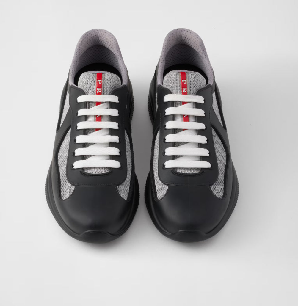 Pair of black and gray sneakers with white laces and a red vertical stripe on the tongue displaying the brand name "Prada".