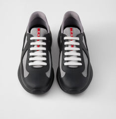 Pair of black and gray sneakers with white laces and a red vertical stripe on the tongue displaying the brand name "Prada".