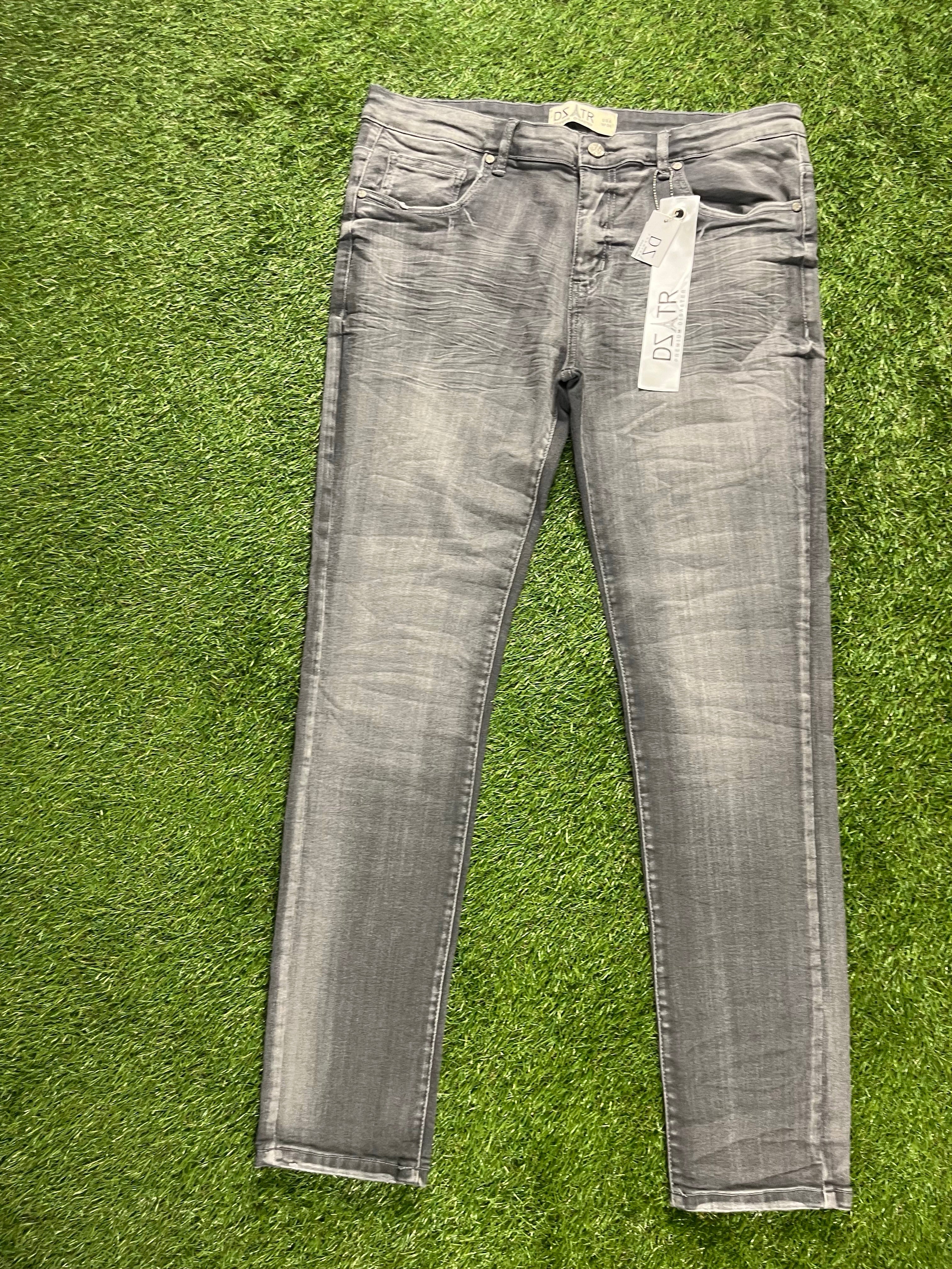 Gray skinny denim jeans with a distressed finish and attached brand tag, set against a grassy background.