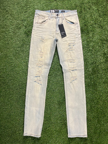 Light-wash distressed skinny jeans with ripped details on the front, displayed flat on a green grass background, waist size 28.