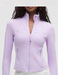 Woman wearing fitted pastel purple zip-up jacket with high collar and long sleeves, paired with white bottoms against a neutral background.