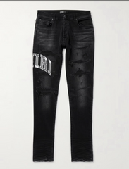 Black distressed slim-fit jeans with rips and white "AMIRI" text on the left thigh, featuring front and back pockets.