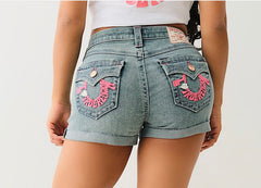 Back view of a person wearing light denim shorts with pink "True Religion" embroidery on pockets and a white cropped shirt.