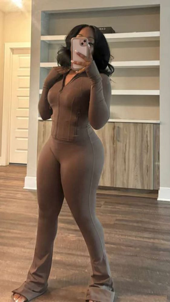 Woman taking mirror selfie wearing tight brown zip-up top and matching high-waisted pants with thumb holes and flared bottoms.