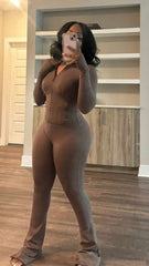 Woman taking mirror selfie wearing tight brown zip-up top and matching high-waisted pants with thumb holes and flared bottoms.