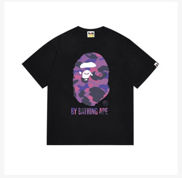 A black t-shirt featuring a purple and pink camouflage BAPE ape face design with the text "BY BATHING APE" underneath.