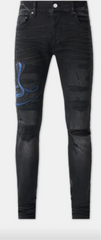 A pair of black distressed skinny jeans with rips on the thighs and a blue snake embroidered on the left leg.