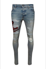 A pair of light blue ripped skinny jeans with distressed details and red snake embroidery on the left thigh.