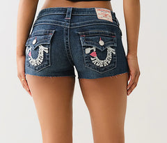 Back view of woman wearing dark denim True Religion shorts with frayed hems and embroidered logo details on both flap-style back pockets.