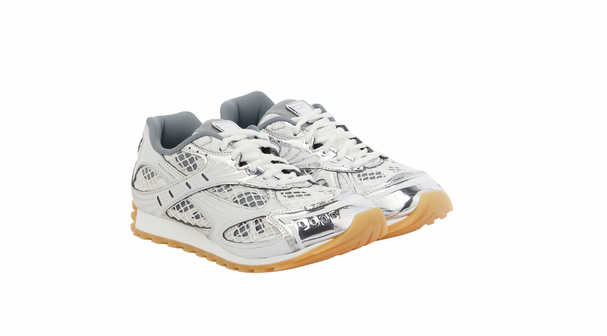 Silver and white sneakers with reflective mesh details, white laces, and a gum sole, displayed from the front.