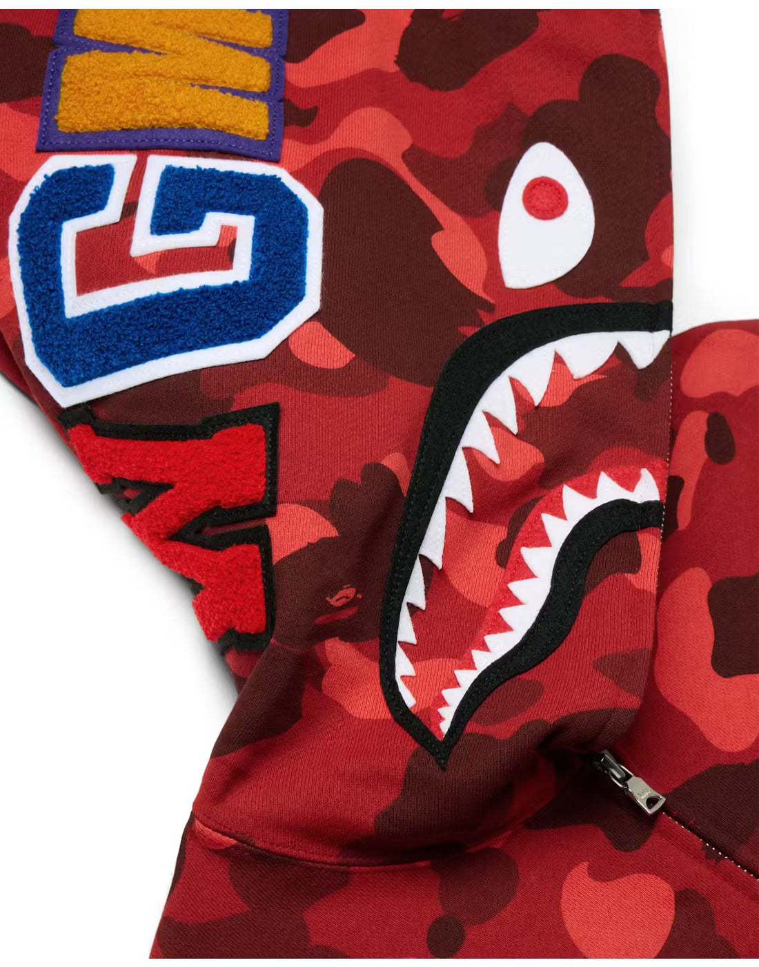 A red BAPE zip-up hoodie with a camouflage pattern, featuring bold eye graphics on the hood and branding on the sleeves.
