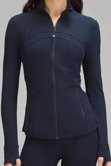Woman wearing fitted black zip-up athletic jacket with curved seam design, thumbholes, and zippered pockets, styled with matching leggings.