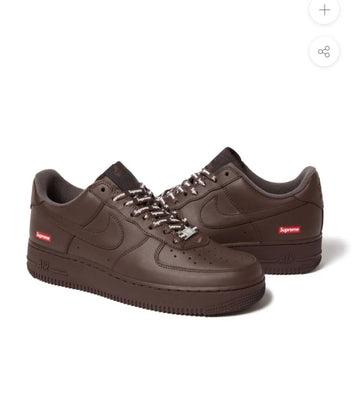 Dark brown Nike Air Force 1 sneakers with Supreme logos on sides, white Supreme branded laces, and black detailing on tongue and sole.