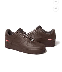 Dark brown Nike Air Force 1 sneakers with Supreme logos on sides, white Supreme branded laces, and black detailing on tongue and sole.