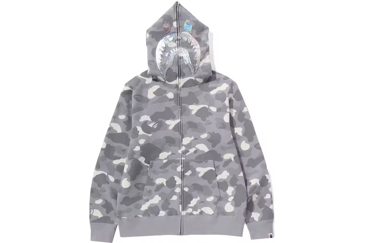 A gray camouflage BAPE hoodie with a shark face graphic on the hood, featuring a zipper and front pockets.