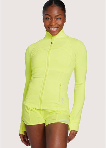 Woman smiles wearing bright neon yellow zip-up jacket and matching shorts, standing against a plain light background.