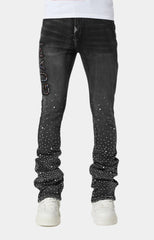 Black jeans with rhinestone embellishments, featuring a “GUAP” design on the left thigh and a slim, stacked fit. Paired with white sneakers.