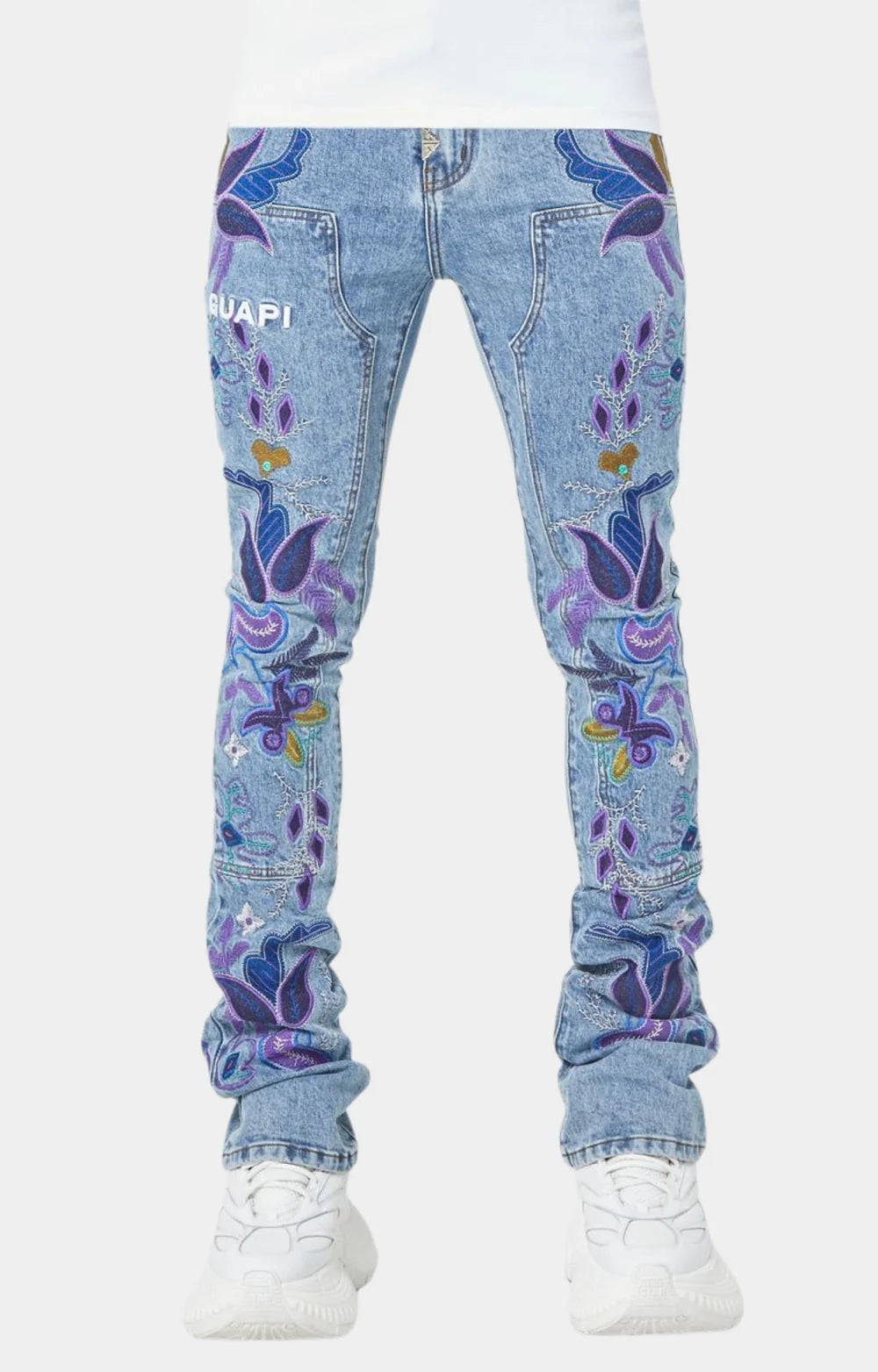 Front view of blue denim jeans with colorful purple and blue floral embroidery worn with white sneakers on a plain white background.