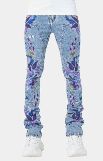 Front view of blue denim jeans with colorful purple and blue floral embroidery worn with white sneakers on a plain white background.