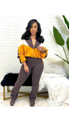 Woman with long black hair wears a yellow and brown zip-up jacket with matching brown pants and sneakers indoors.