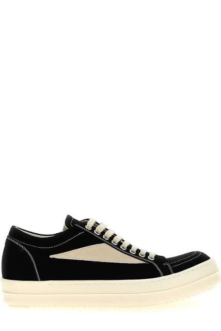 Black sneakers with beige accents and white stitching, featuring a low-profile design and cream-colored sole, displayed from the side.