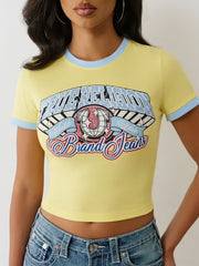 Woman wearing a yellow cropped t-shirt with blue ringer accents and a colorful graphic that says “True Religion Brand Jeans.”