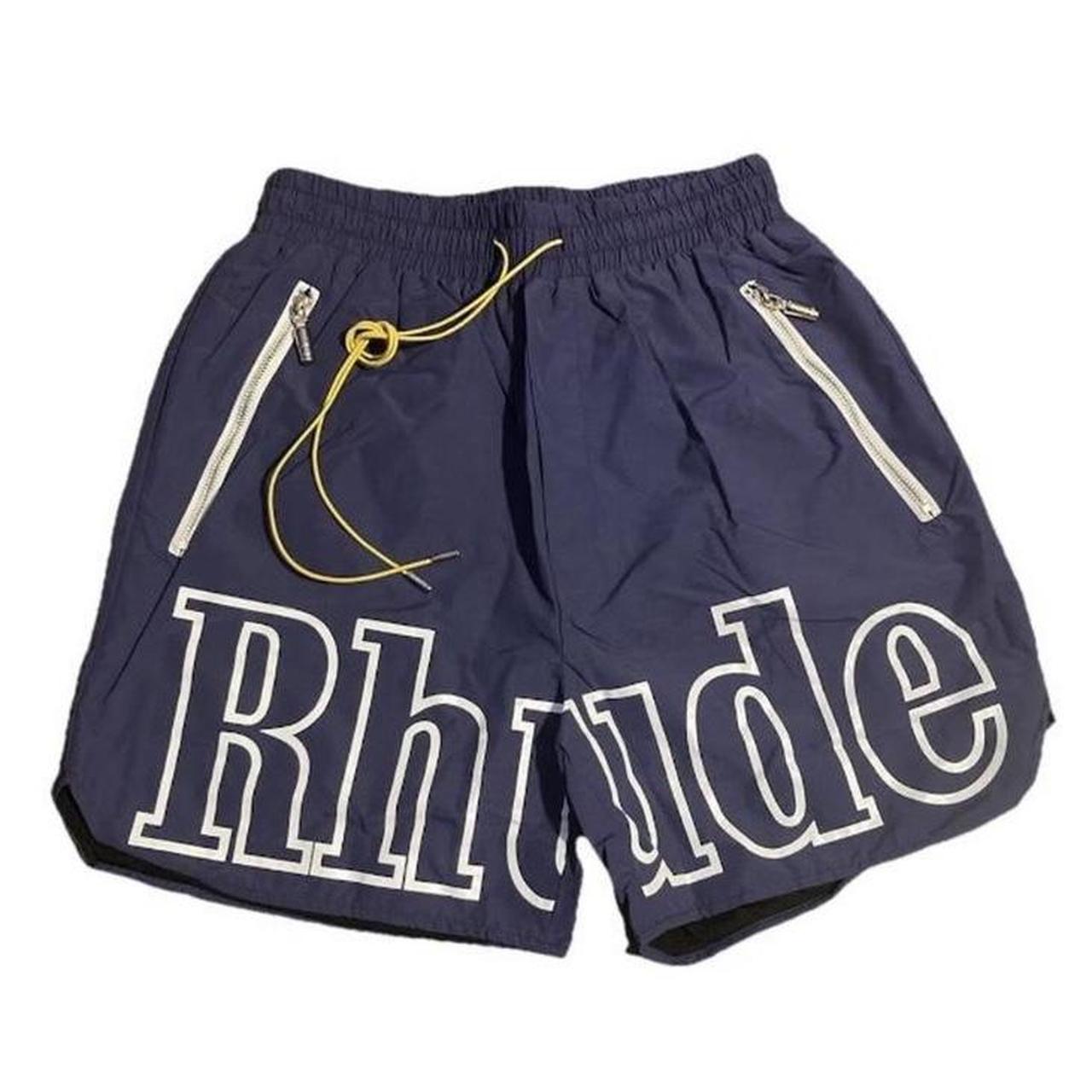 Navy blue Rhude shorts with white outlined logo across the front, yellow drawstrings, and silver zippered pockets on both sides.