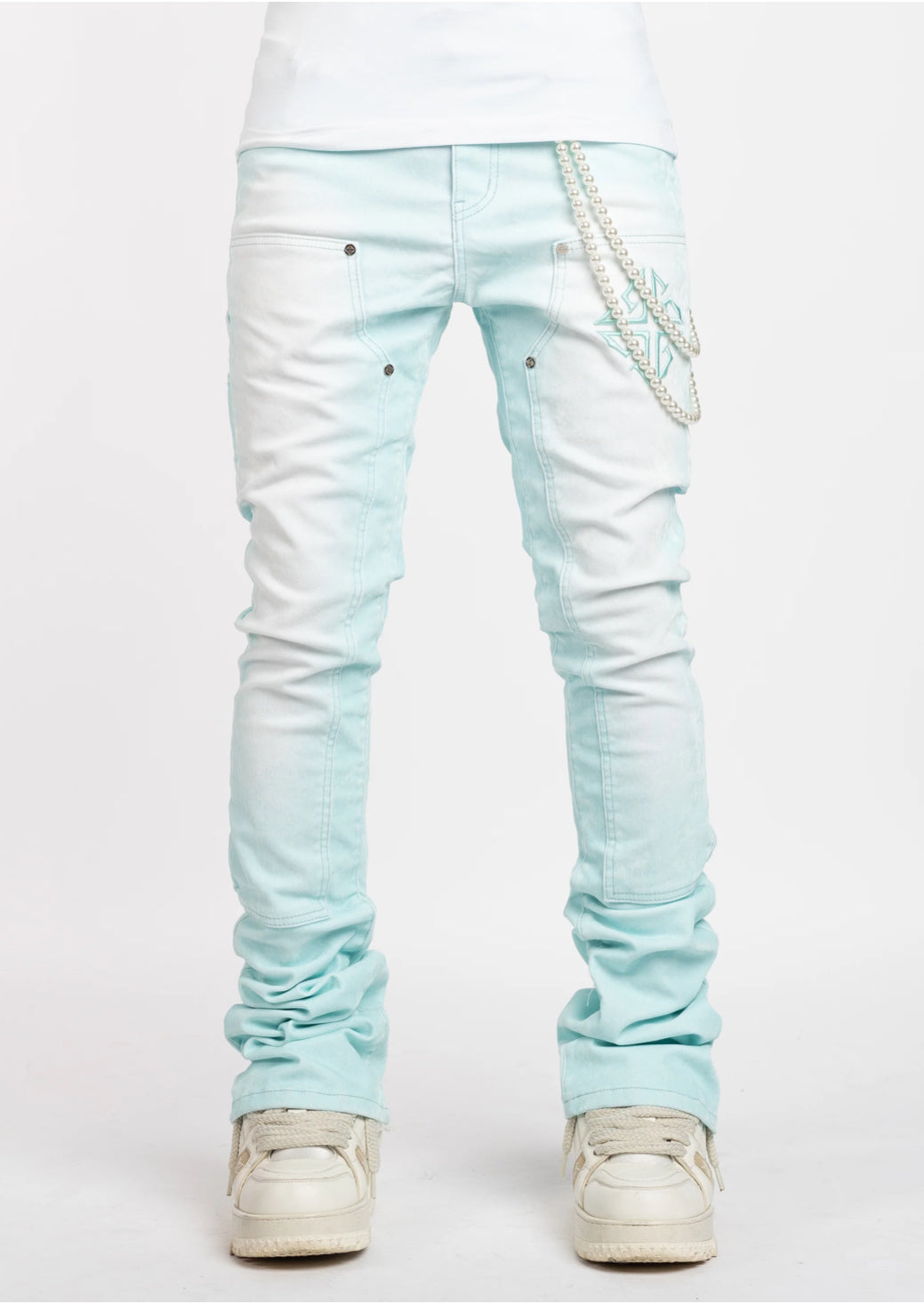 Front view of light blue skinny jeans with stitched details and pearl chain accessory, paired with white sneakers.