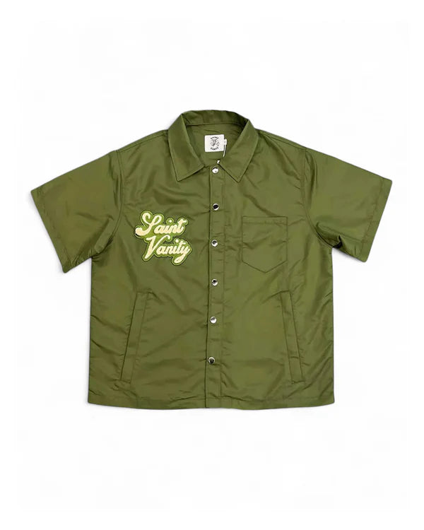 A short-sleeved olive green jacket with a "Saint Vanity" logo embroidered on the left chest, featuring a button-up closure.