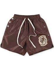 A pair of brown Saint Vanity shorts with a logo patch on the front, snap button details on the sides, and an elastic waistband.
