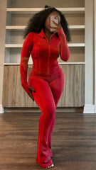 Woman wearing fitted red zip-up two-piece set with long sleeves and flared pants, taking mirror selfie in modern room with wood floors.