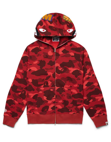 A red BAPE zip-up hoodie with a camouflage pattern, featuring bold eye graphics on the hood and branding on the sleeves.