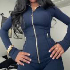 A woman wearing a navy blue zip-up athletic jacket with a fitted design, standing with hands on hips, showcasing a casual look.