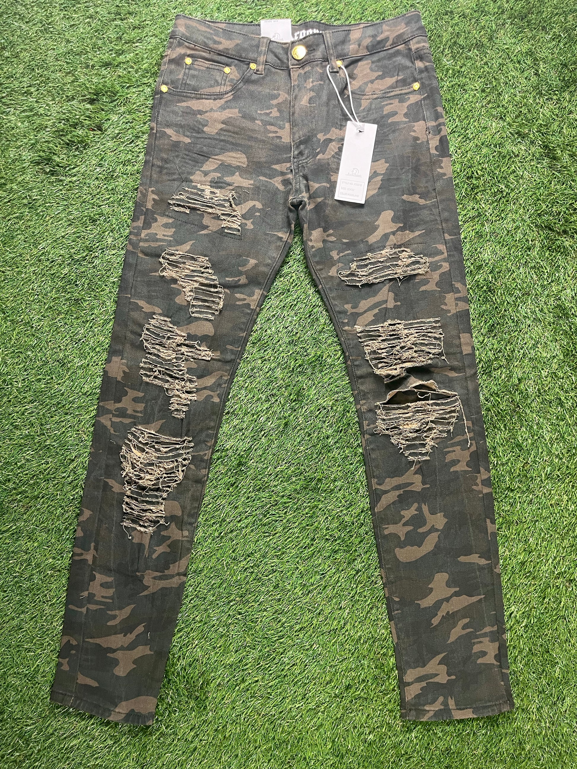 A pair of camo-patterned skinny jeans with multiple distressed rips, yellow button details, and price tags attached.