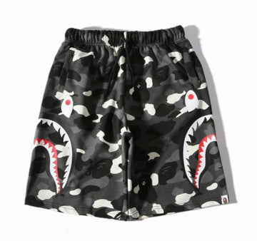 A pair of black BAPE camouflage shorts with large shark mouth graphics on both sides, featuring a drawstring waist and side pockets.