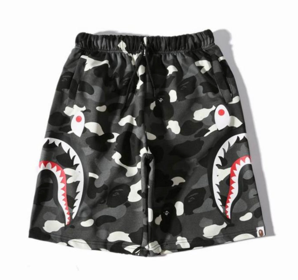 A pair of black BAPE camouflage shorts with large shark mouth graphics on both sides, featuring a drawstring waist and side pockets.