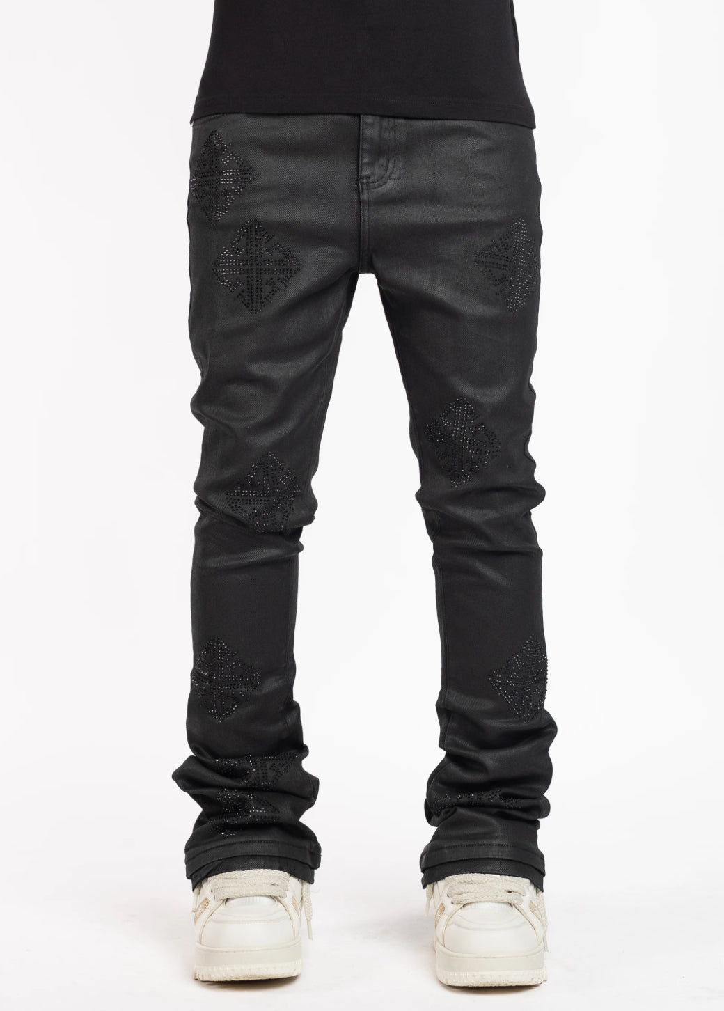 Man wearing black skinny jeans with textured diamond-shaped patterns and white sneakers, standing against a plain white studio background.