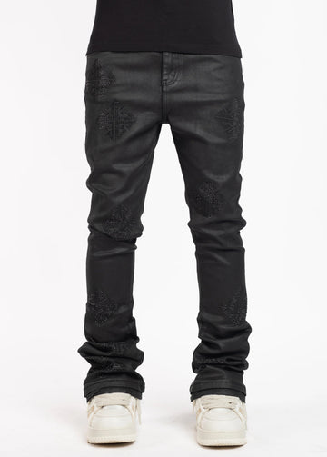 Man wearing black skinny jeans with textured diamond-shaped patterns and white sneakers, standing against a plain white studio background.