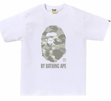 A white t-shirt featuring the BAPE logo, with a camouflage ape face design and the text "BY BATHING APE" underneath.