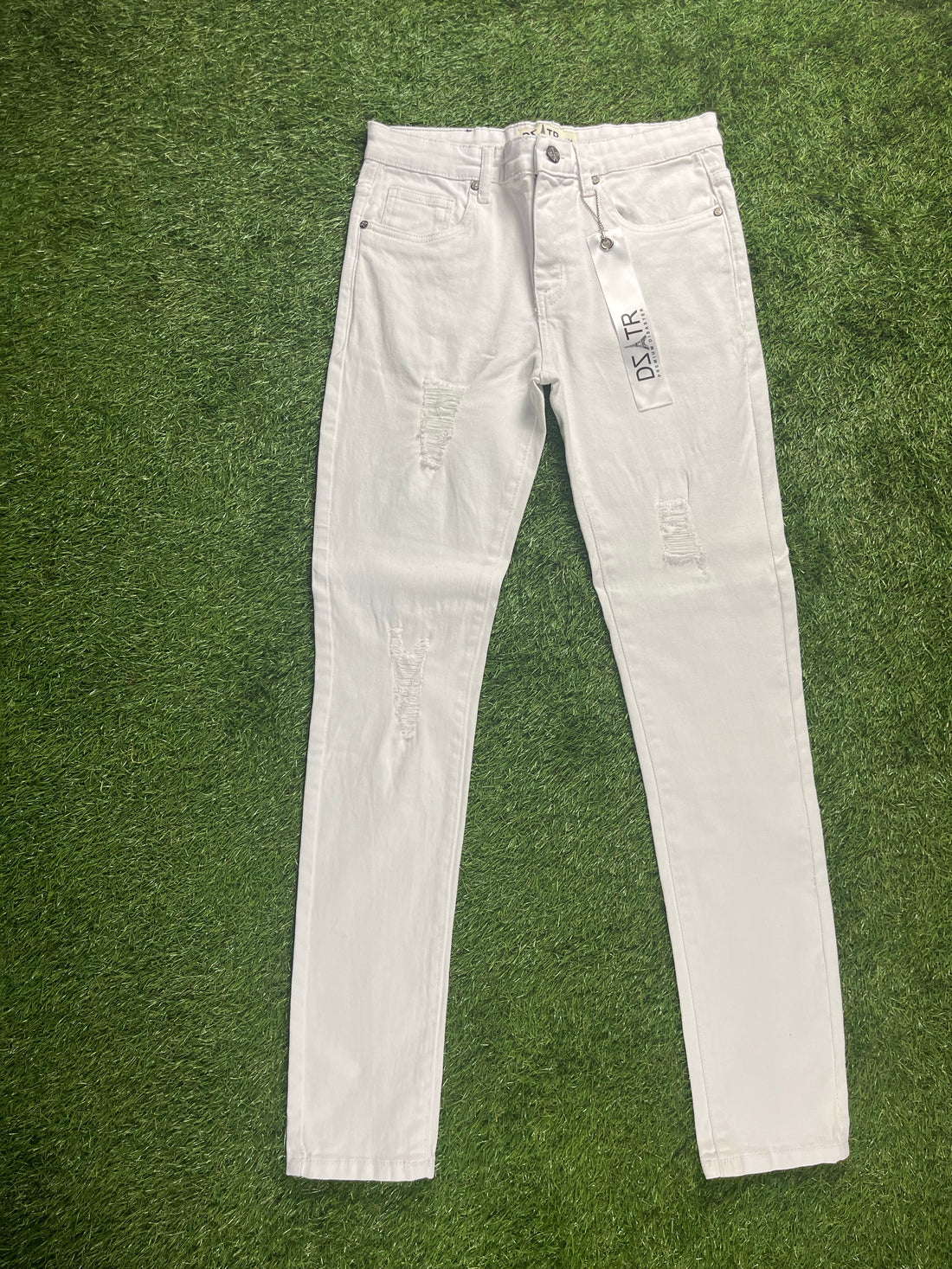 A pair of white skinny jeans with distressed detailing on the front, featuring tags attached to the waistband.