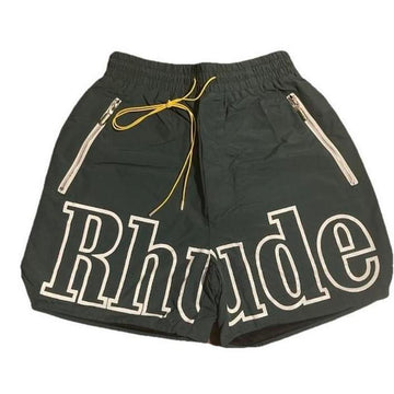 Black shorts with large white outlined "Rhude" text on the front, yellow drawstring, and white zipper pockets on each side.