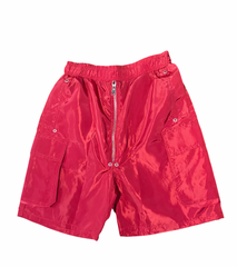 Bright red shiny nylon shorts with elastic waistband, silver zipper front, and large flap pockets on each side against white.