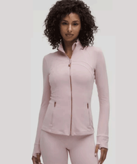 Woman with curly hair wearing light pink zip-up jacket and matching pants, posing against plain light gray background.