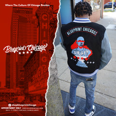 Person wearing a black and gray varsity jacket with “Blueprint Chicago” text and graphic art, standing on a city sidewalk.